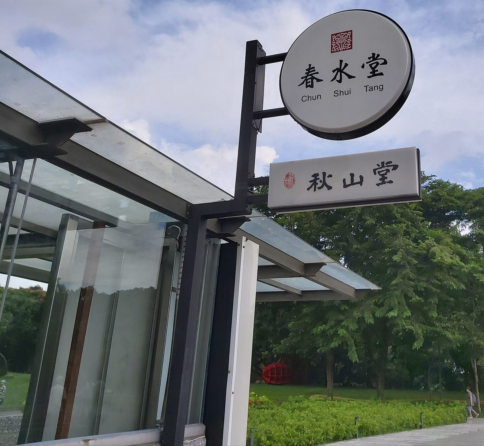 圓形吊掛招牌上寫著大大的「春水堂」三個字，底下一行小字 Chun Shui Tang，下方另掛一塊秋山堂的招牌
