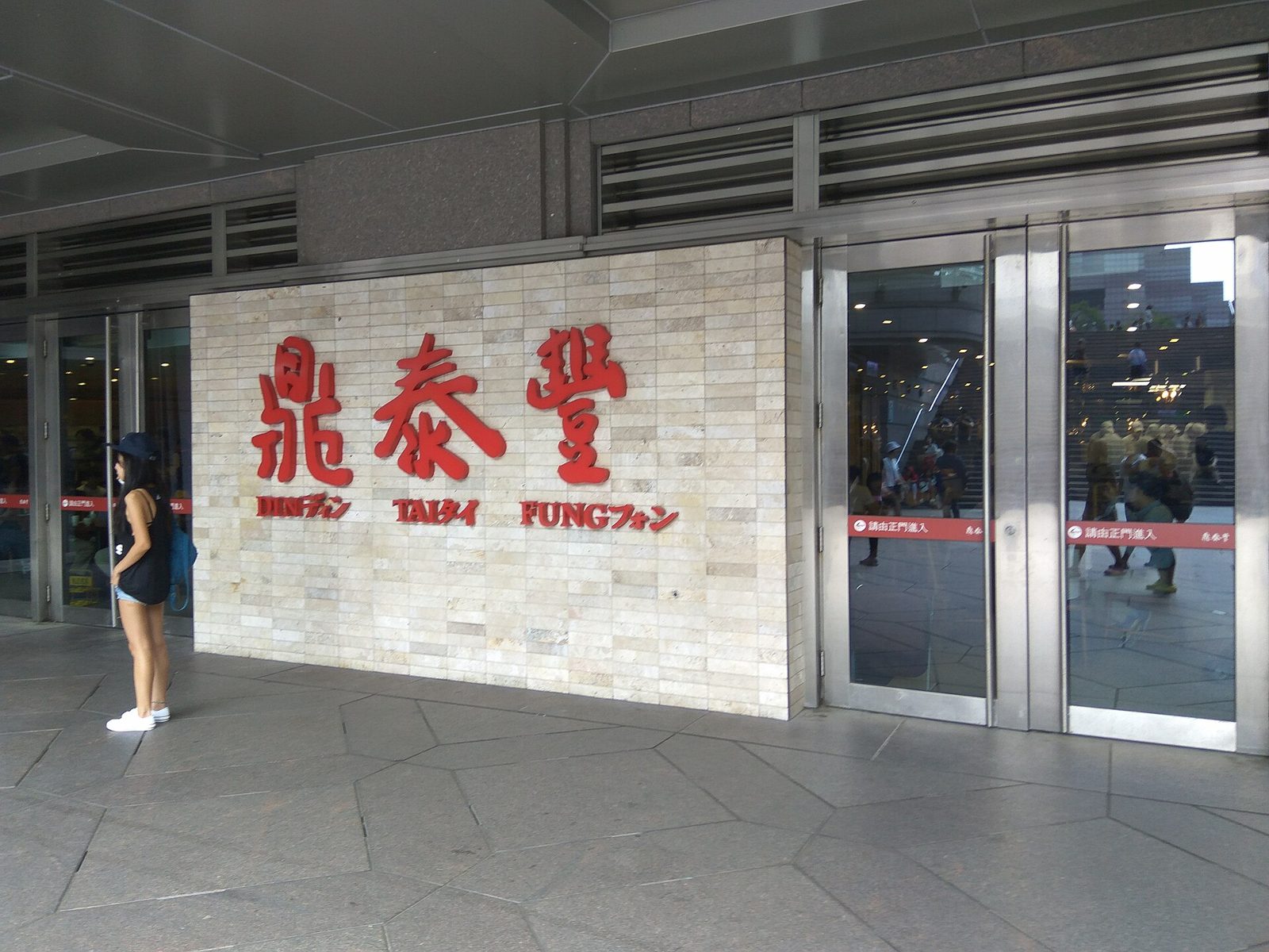 石牆上掛著紅色立體字「鼎泰豐」，底下一排較小的紅字 DIN TAI FUNG，每個英文字旁邊並列日文片假名
