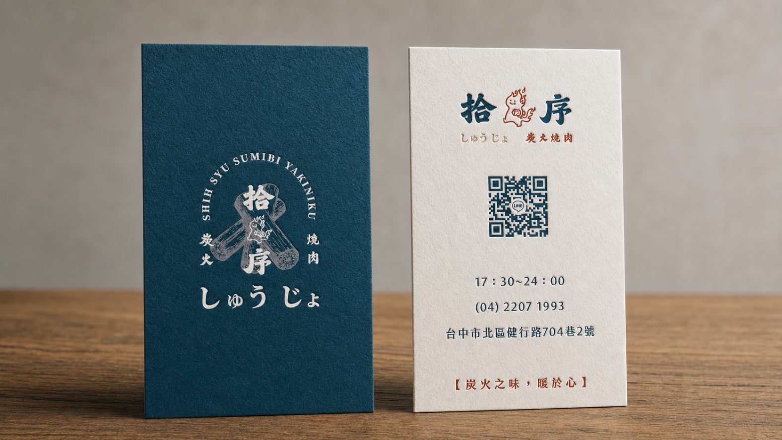 兩張直式名片立在木桌上，深藍色那張的 SHIH SYU SUMIBI YAKINIKU 繞成弧形圍著拾序標誌，白色那張印著店名、營業時間與地址
