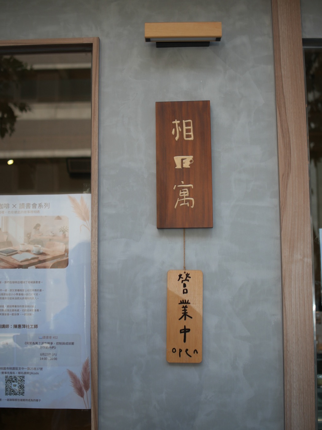咖啡店的木質直式門牌，店名與圖形刻進木頭裡，下方掛著營業中的小木牌