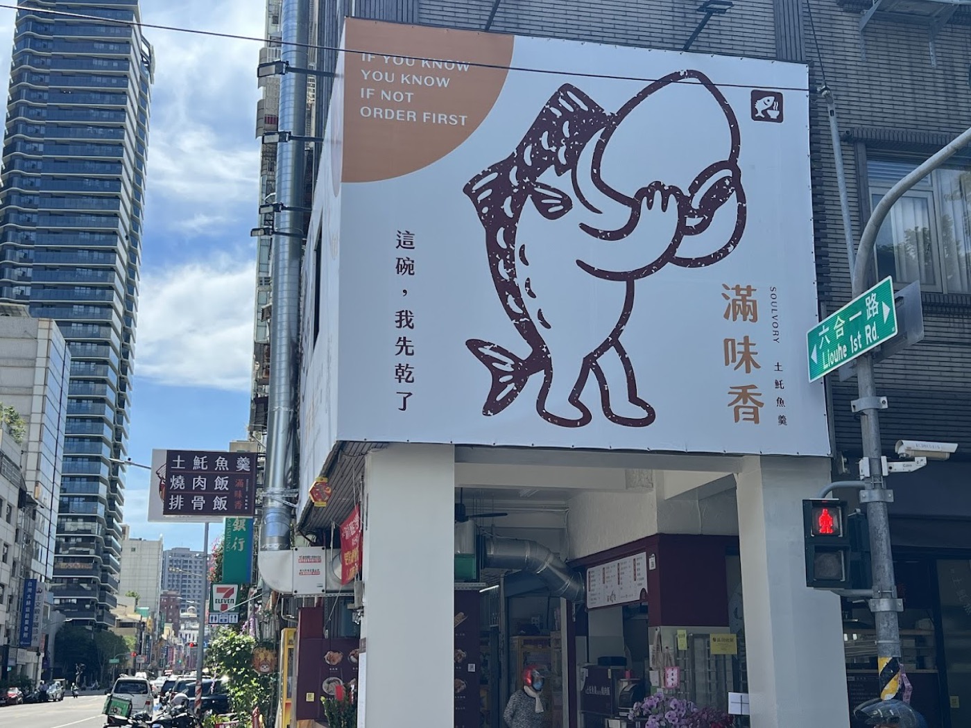 滿味香外牆招牌上的吉祥物，一尾雙手捧碗、站著喝湯的土魠魚，旁邊直排店名