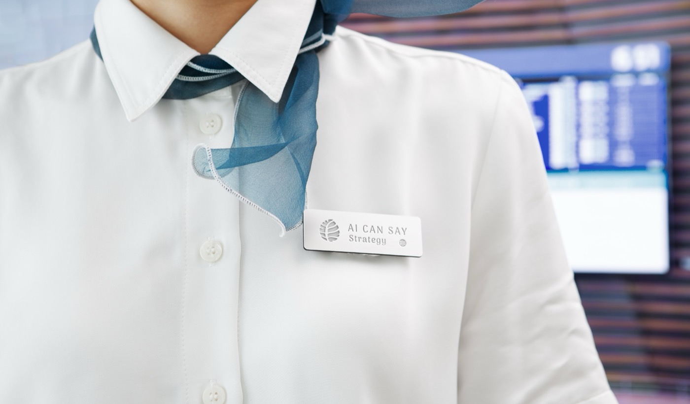 白襯衫制服胸前的金屬名牌，標誌與文字縮在只有幾公分寬的牌面上