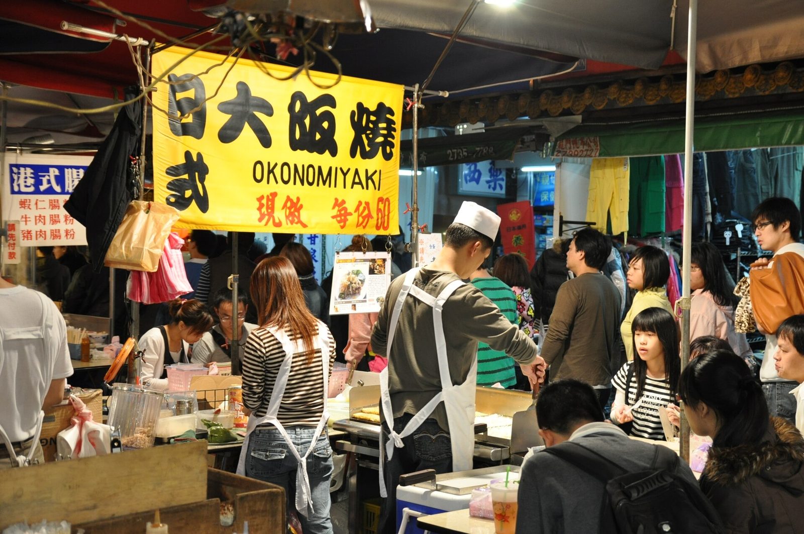 饒河街夜市的攤位，黃色招牌上寫著日式大阪燒和現做，攤前圍著排隊的客人
