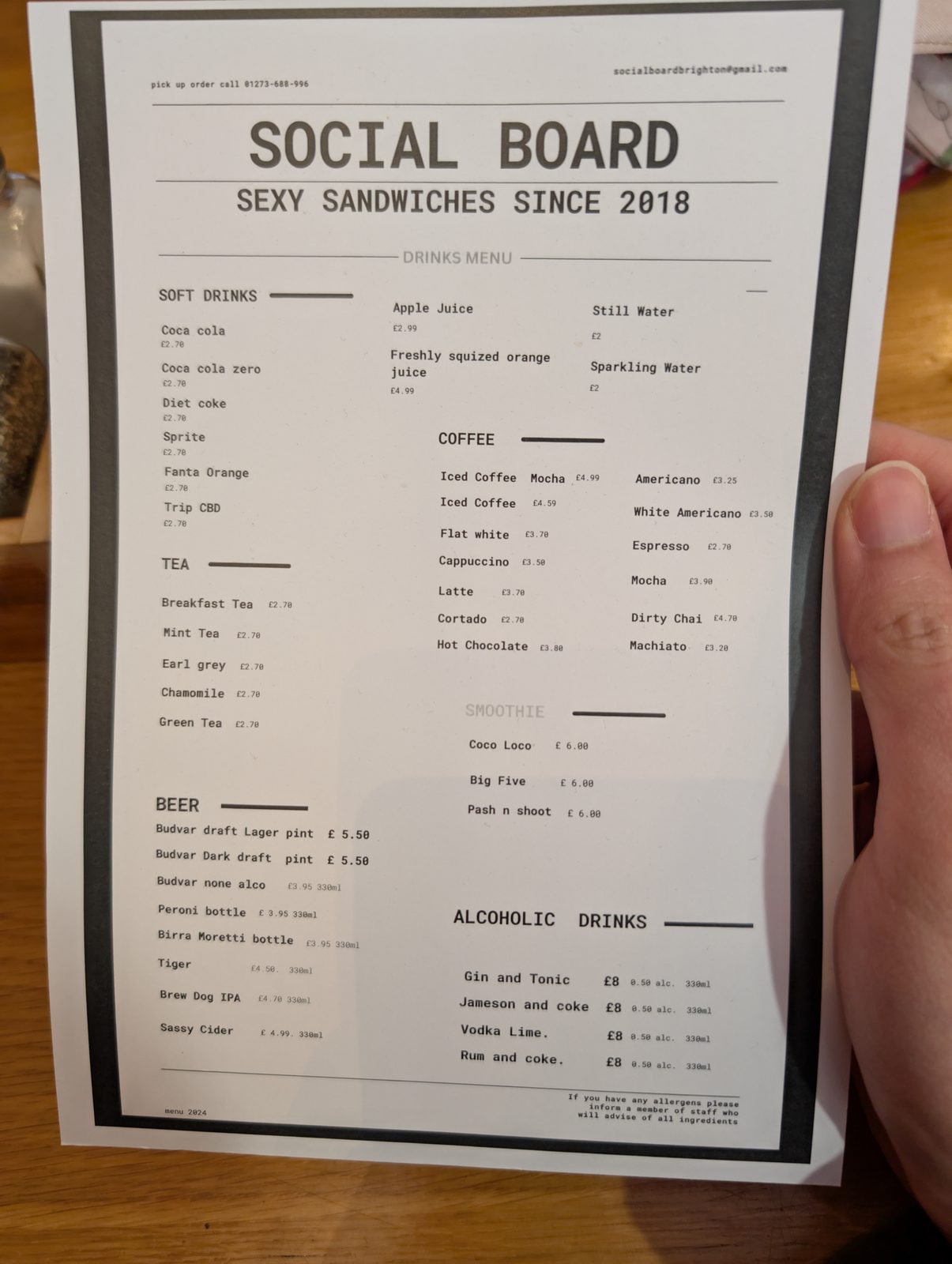 手拿著一張印好的飲料菜單，分成軟性飲料、咖啡、茶等區塊，每區的品項沿著同一條左邊線往下排