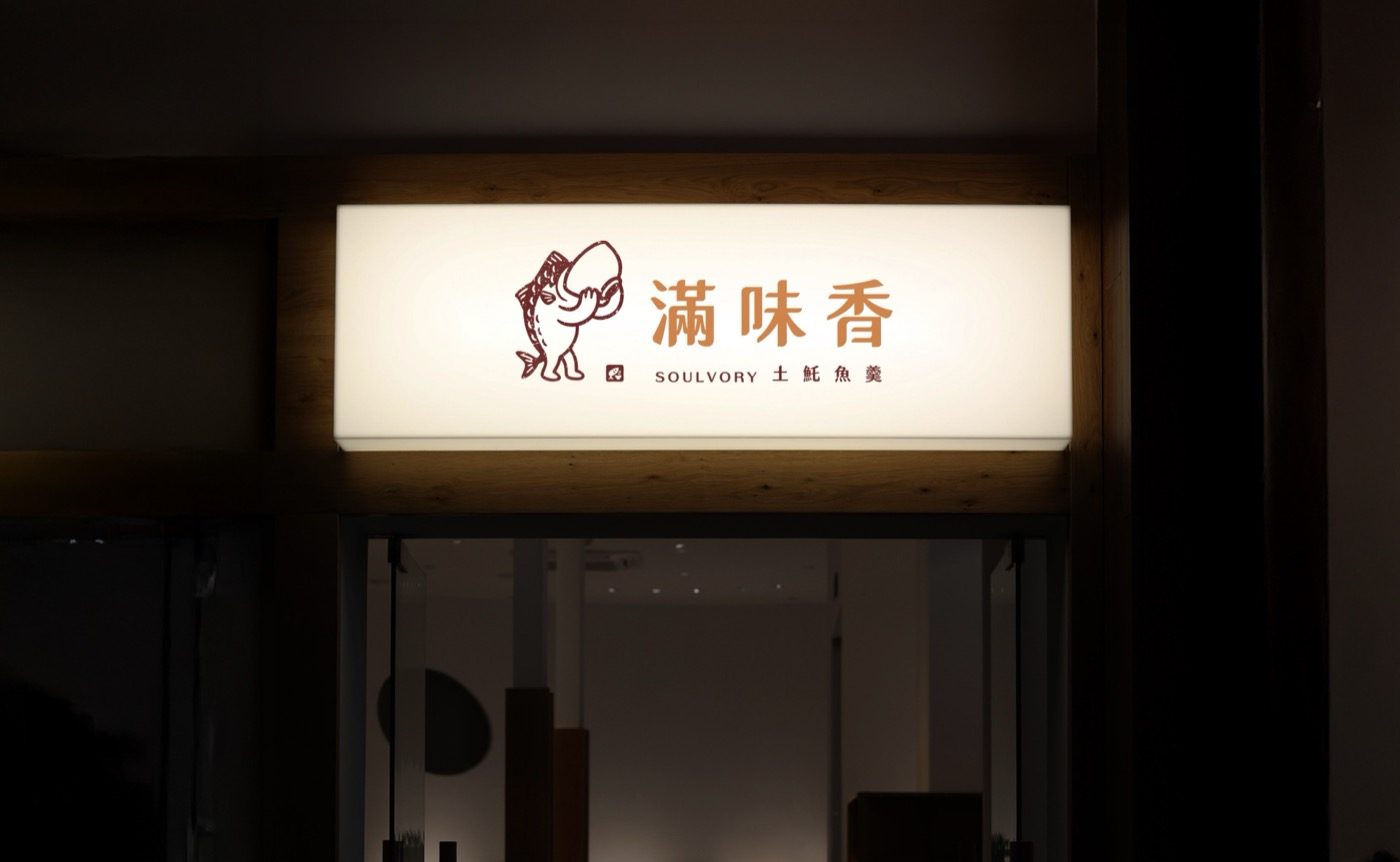夜裡店門上方的白色燈箱發亮，燈箱上是魚角色與滿味香店名，周圍一片暗