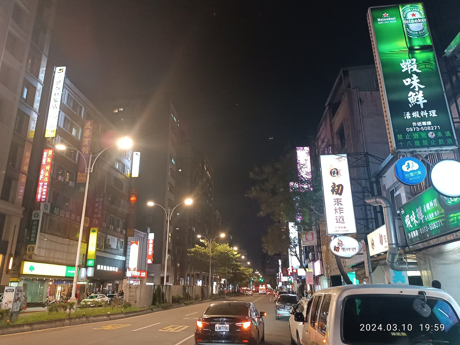 夜晚的台北松山街道，路燈與車燈之間，幾塊直式發光招牌亮著，其他沒有燈的招牌跟建築一起暗下去
