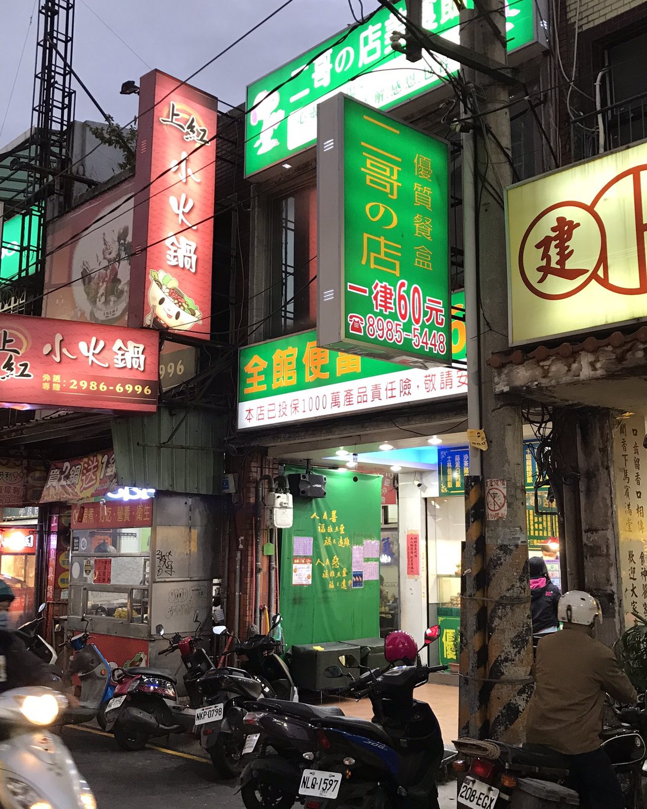 傍晚的台北街道，騎樓上方一整排店家招牌，紅綠黃白各種顏色疊在一起，騎樓下停滿機車