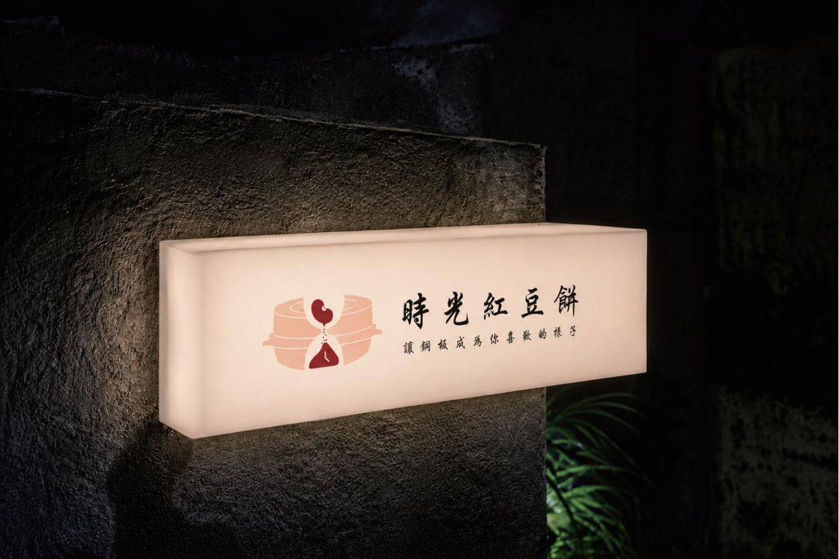 夜裡石牆上亮著的橫式燈箱,左邊紅豆餅圖形,右邊時光紅豆餅店名與標語