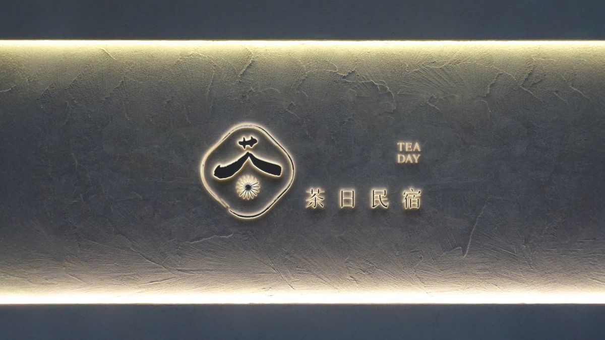 上下打光的灰牆上，發光的茶日民宿 Logo 與標準字