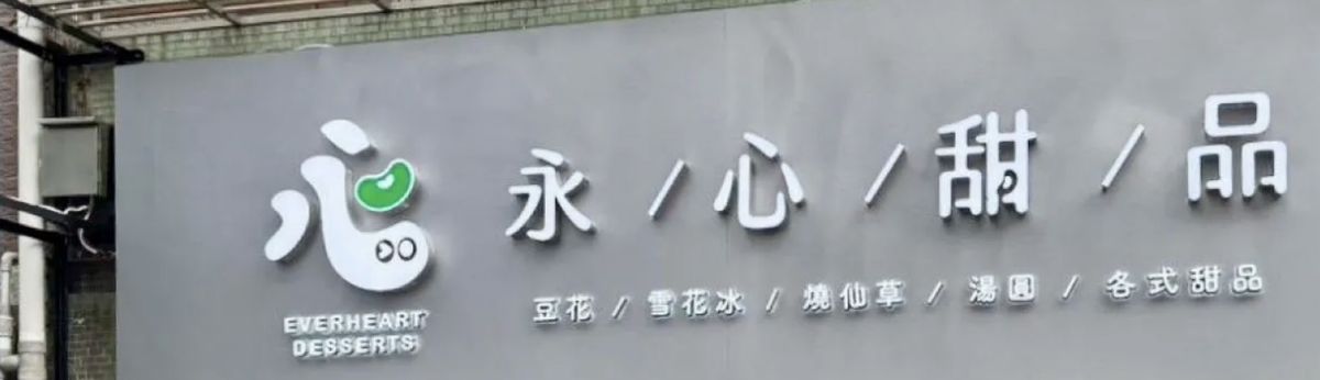 永心甜品實際店面的灰色橫式招牌,白色立體字與綠色豆子圖形,下排寫著豆花、雪花冰、燒仙草、湯圓