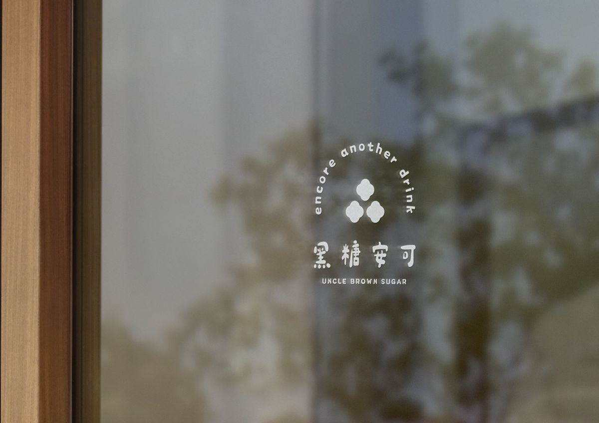 玻璃窗上的白色黑糖安可 Logo 窗貼，映著窗外樹影