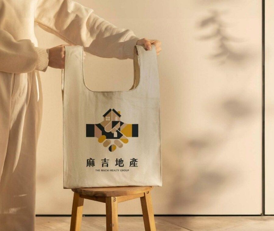 有人提著米白帆布袋放在木凳上,袋上印著彩色麻吉地產 Logo