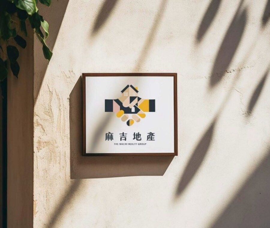 米白灰泥牆上的木框招牌,裡面是彩色握手房屋 Logo 與麻吉地產