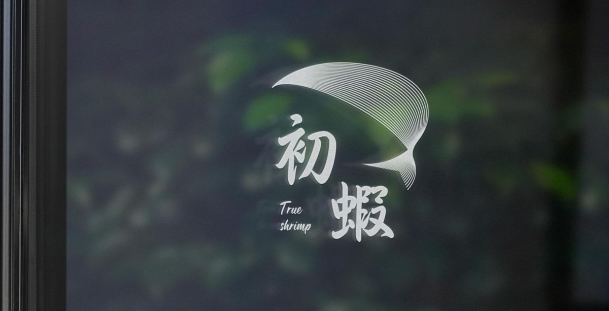 白色的初蝦標誌貼在玻璃窗上,後面是模糊的綠色植物
