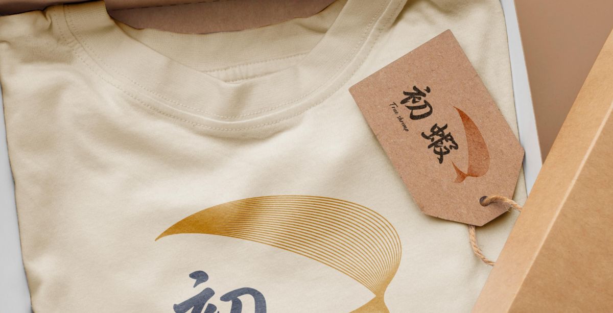 米色 T 恤印著金色的初蝦標誌,旁邊掛著牛皮紙吊牌